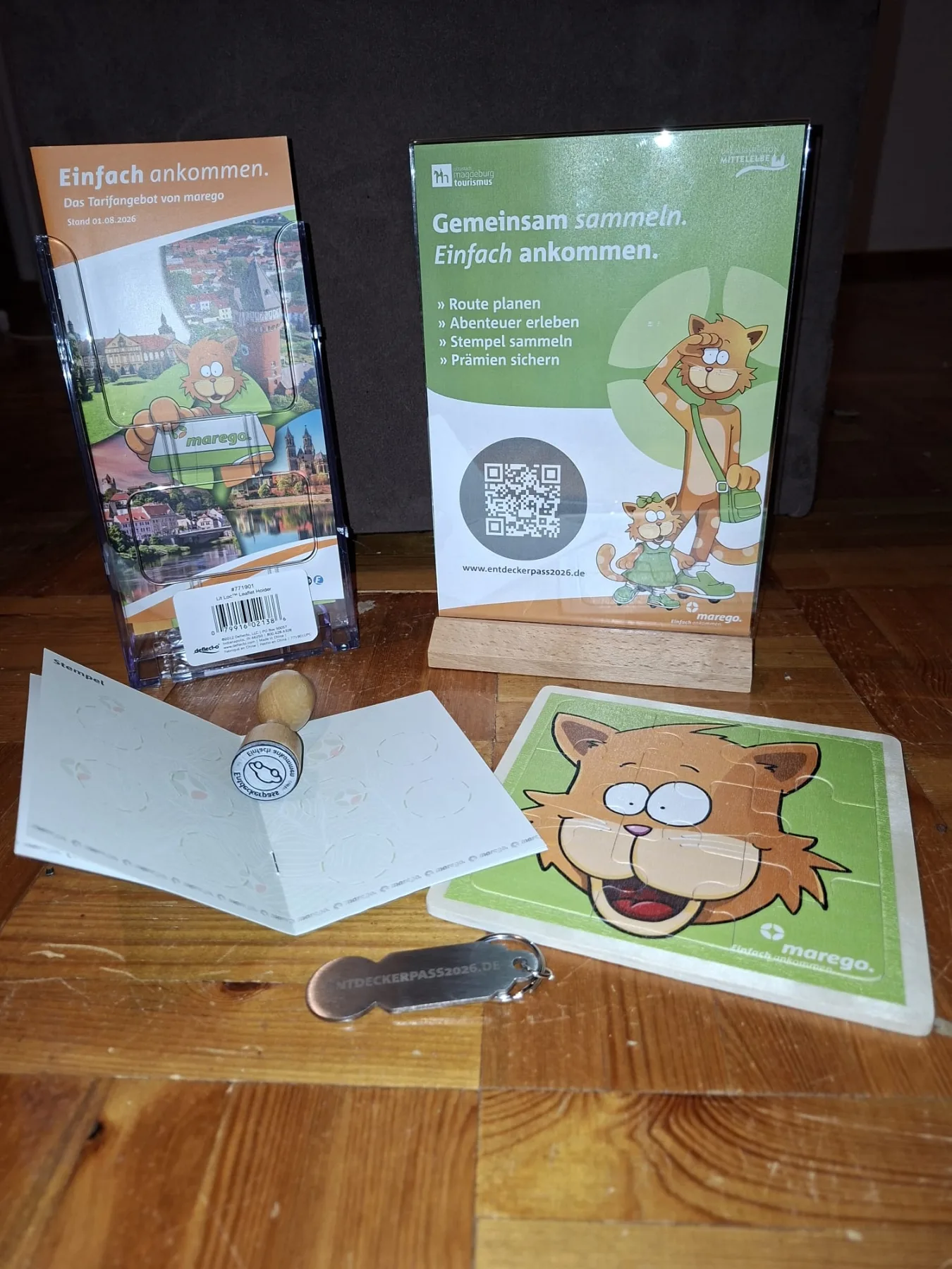 Entdeckerpass-Materialien am FuMinGo-Kiosk: marego-Aufsteller, aufgeschlagenes Stempelheft mit dem FuMinGo-Stempel, Holzpuzzle und Einkaufswagenchip