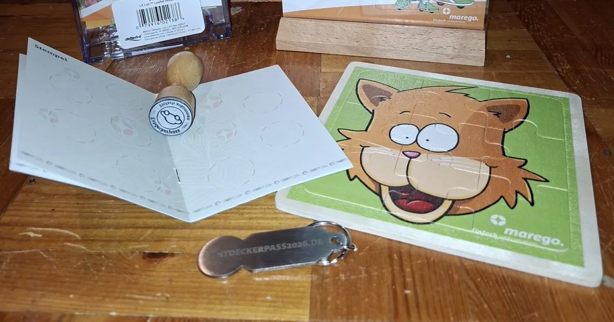 Stempelheft des Entdeckerpasses mit dem FuMinGo-Stempel, dazu Holzpuzzle und Einkaufswagenchip